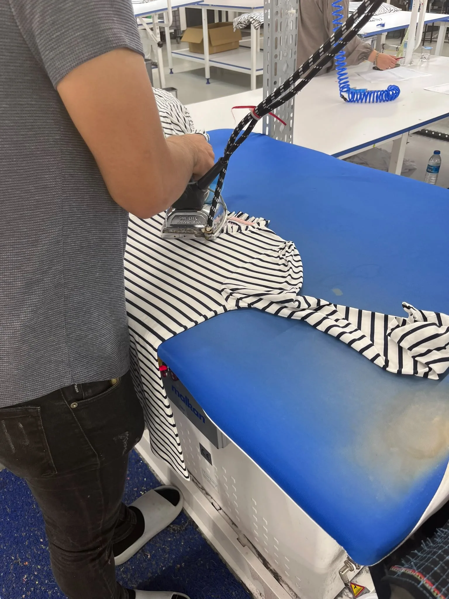 Mavi ütü masasında buharla ütülenen çizgili bir triko