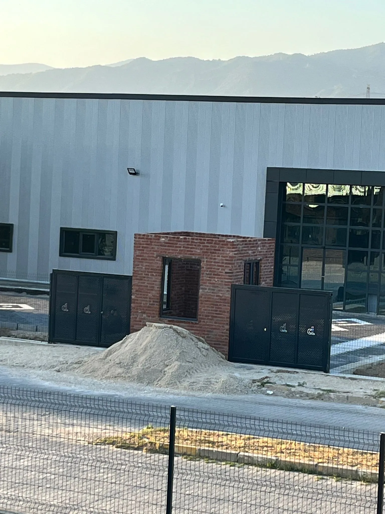 Erbaa'daki çelik kaplı ikinci Darsateks fabrikası ve önündeki küçük tuğla giriş binası; ufukta dağlar